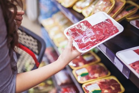 person looking at package of raw meat in supermarket
